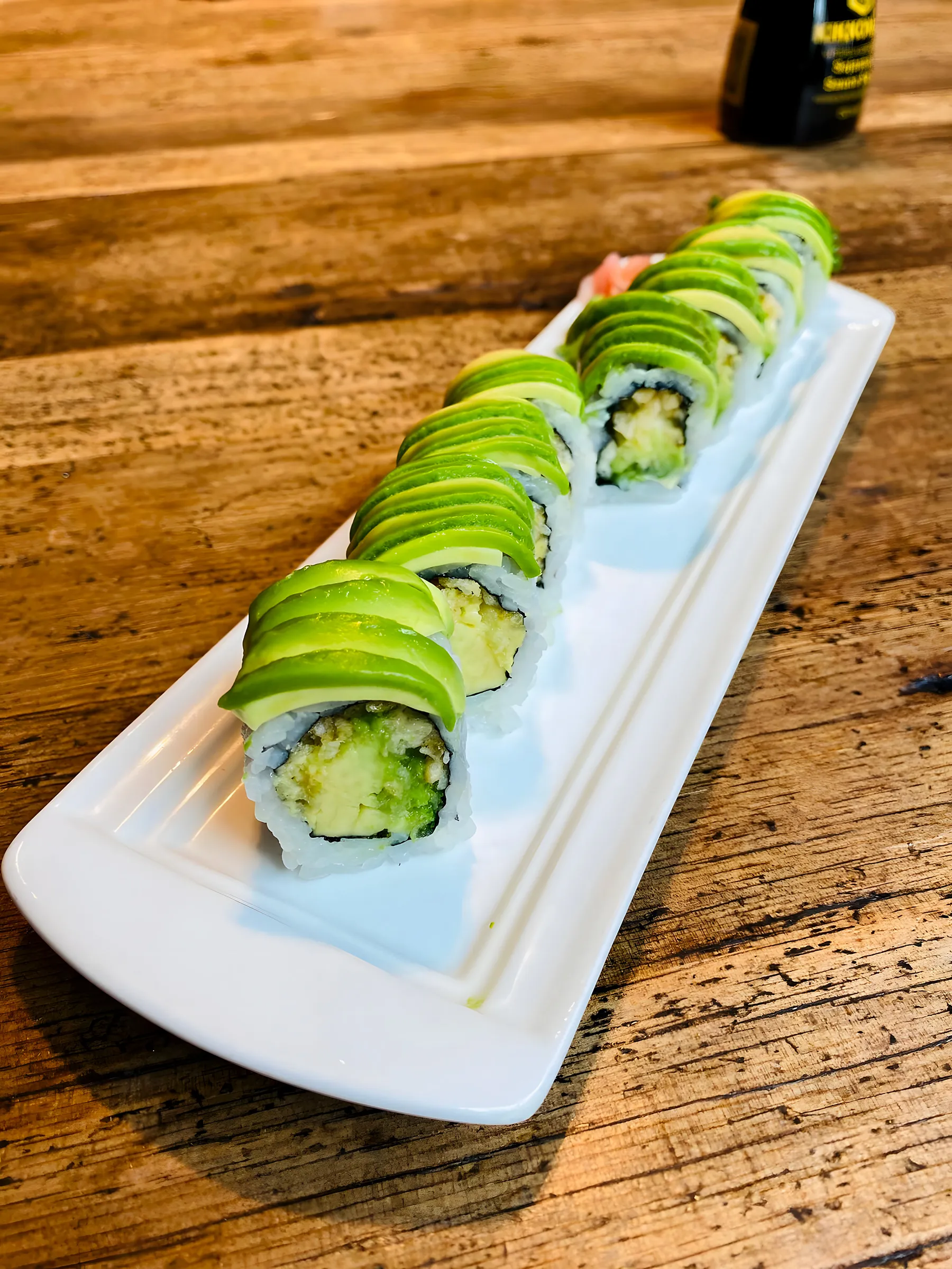 Groene avocado-roll op een lang wit bord op houten tafel